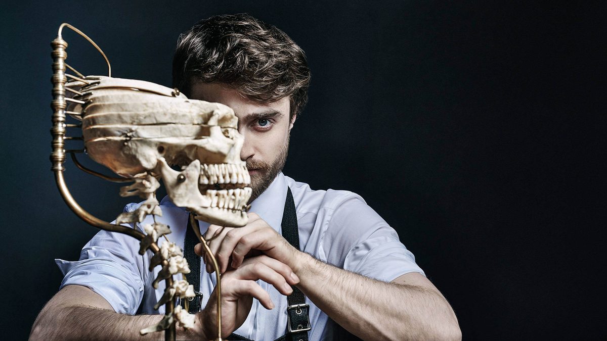 Daniel Radcliffe poses behind a skull on black background