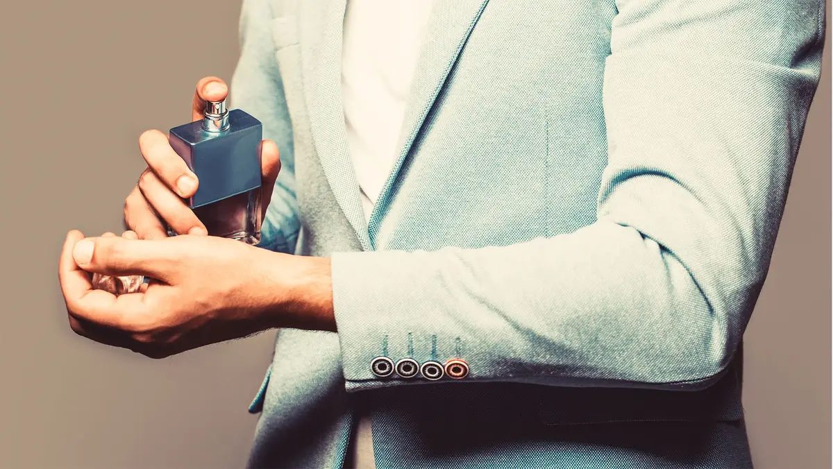 Man in light gray suit spraying cologne onto his inner wrist
